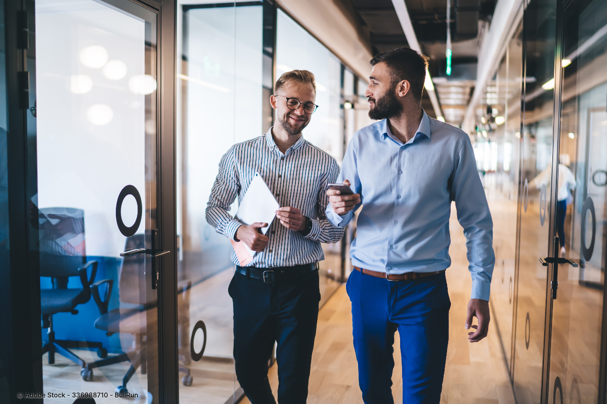 Zwei Männer in Hemden und Stoffhosen gehen durch ein modernes Büro und präsentieren stilvolle Business Casual für Herren Outfits.